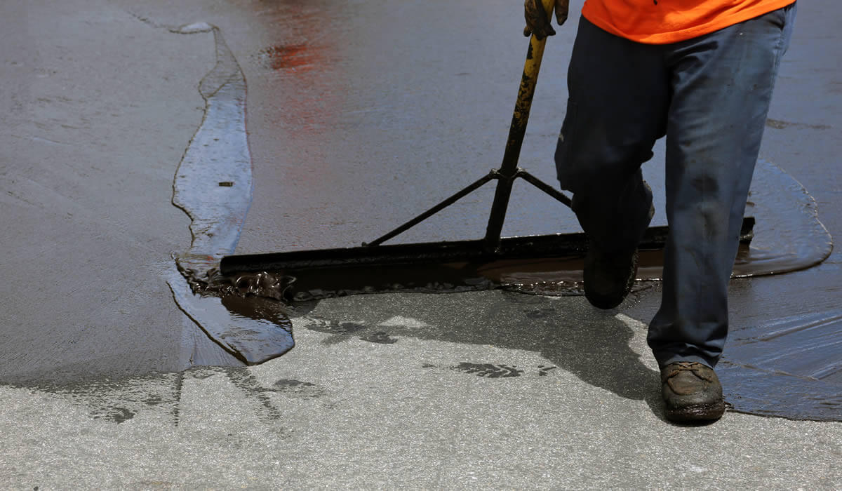 man using a spreading tool to seal a driveway